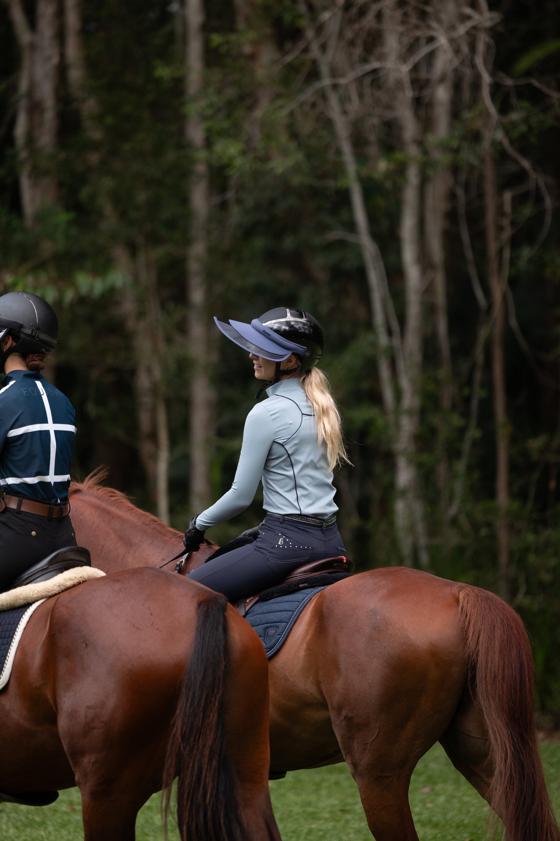 Two people riding horses in a forested area