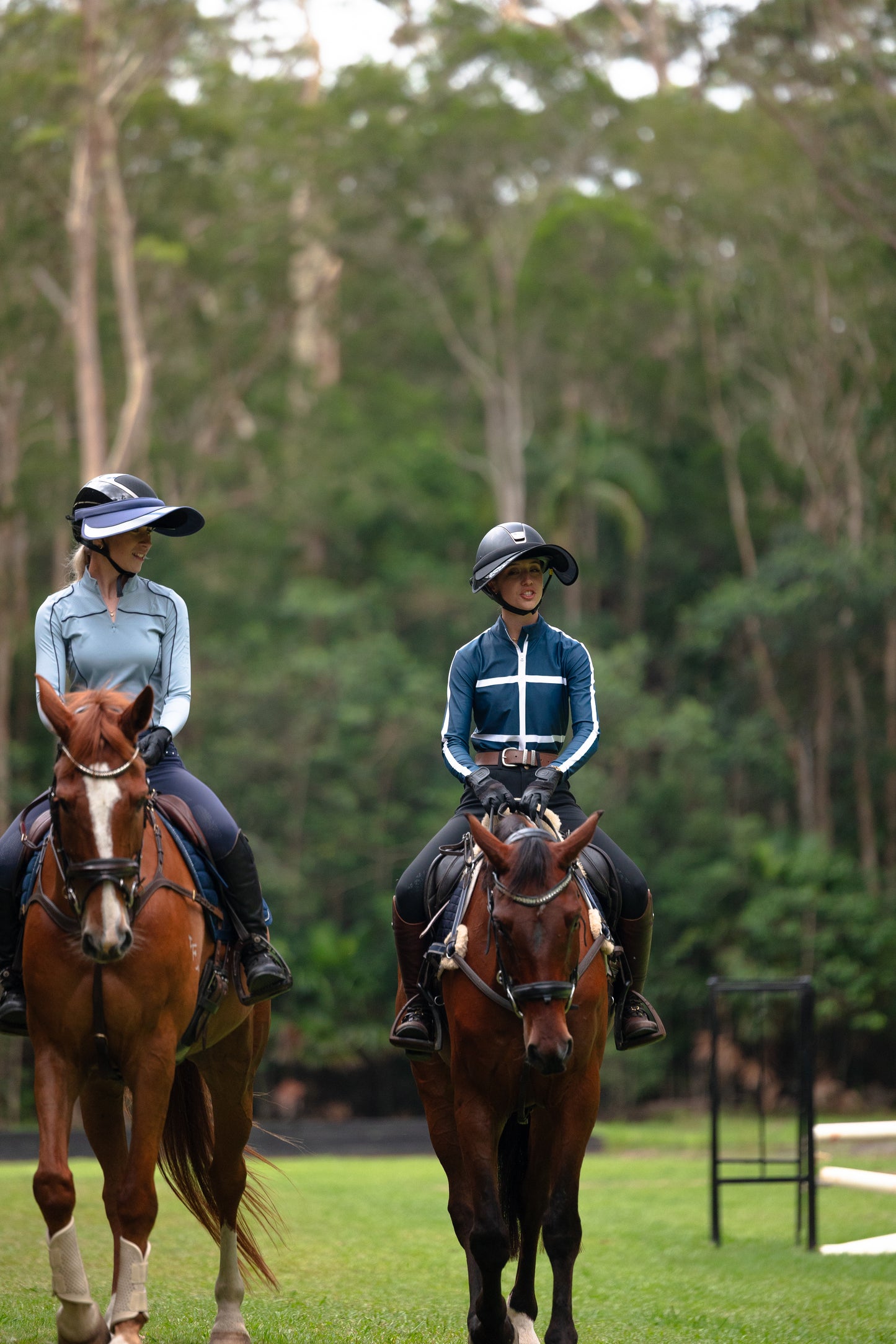 Two people riding horses in a grassy area with trees in the background